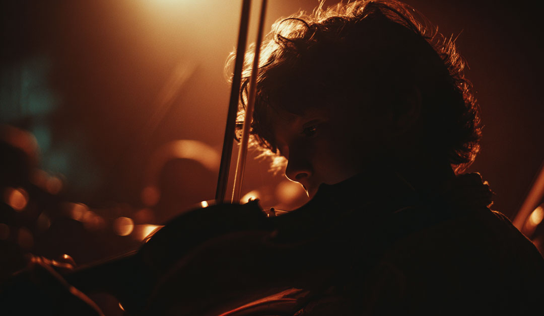 Le regard d'un jeune violoniste qui cherche à jouer la note juste pour s'accorder au reste du groupe